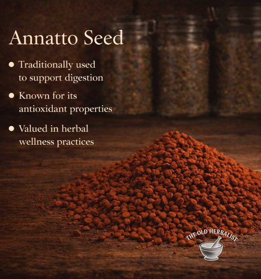 Annatto seed on a wooden surface with text about its uses and The Old Herbalist branding.