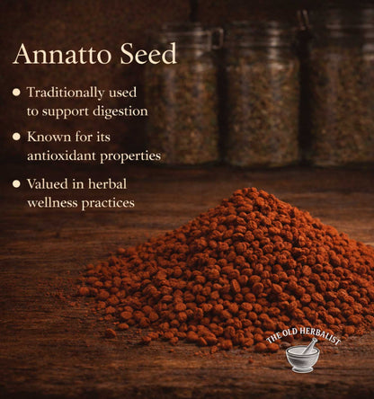 Annatto seed on a wooden surface with text about its uses and The Old Herbalist branding.